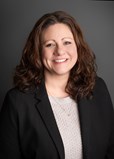 headshot of a smiling woman with curly dark hair dressed in business professional attire